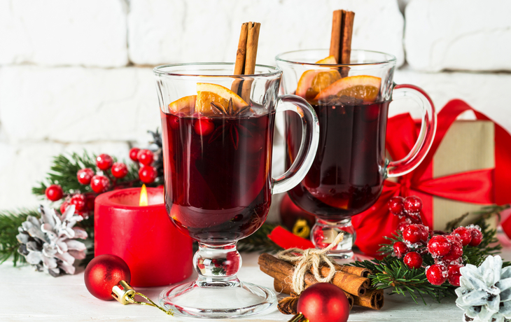 Glühwein im Glasbecher mit Frucht und Gewürzen auf Weiß