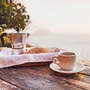 Mittelmeer-Frühstück, Kaffee und frischem Brot auf einem Tisch mit Bäumen und Blick auf das Meer im Hintergrund