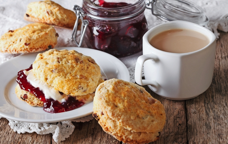 Scones mit Marmelade und Tee mit Milch auf dem Tisch. horizontal